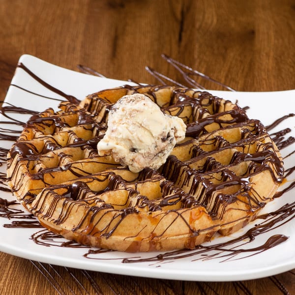 Golden waffle drizzled with chocolate and caramel, topped with a scoop of ice cream.