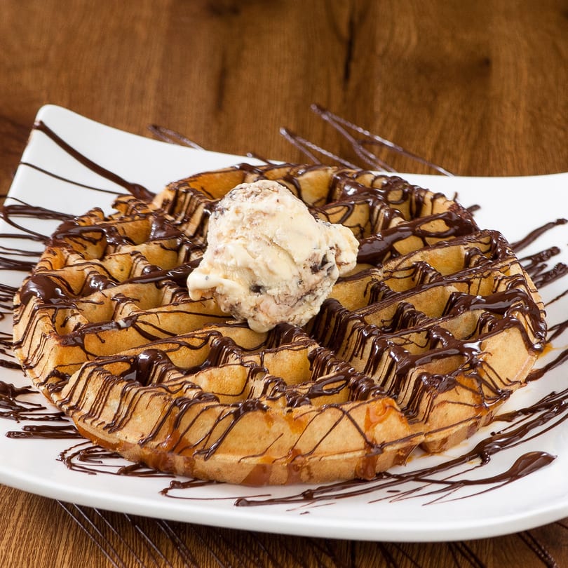 Golden waffle drizzled with chocolate and caramel, topped with a scoop of ice cream.
