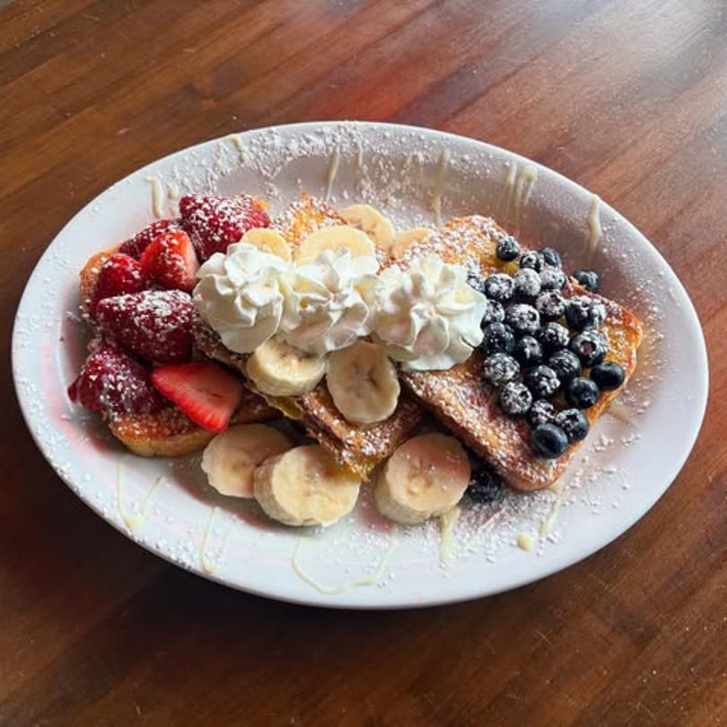 French toast topped with strawberries, blueberries, bananas, whipped cream, and powdered sugar.