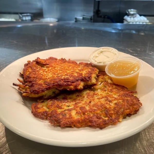 Two golden-brown potato pancakes with sides of applesauce and sour cream on a white plate.