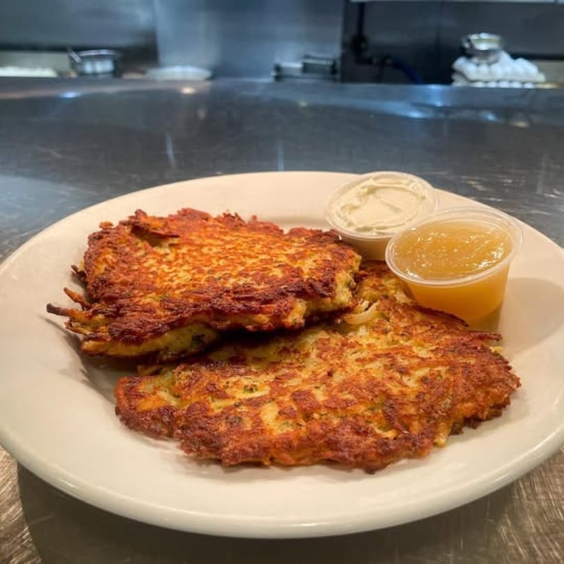 Two golden-brown potato pancakes with sides of applesauce and sour cream on a white plate.