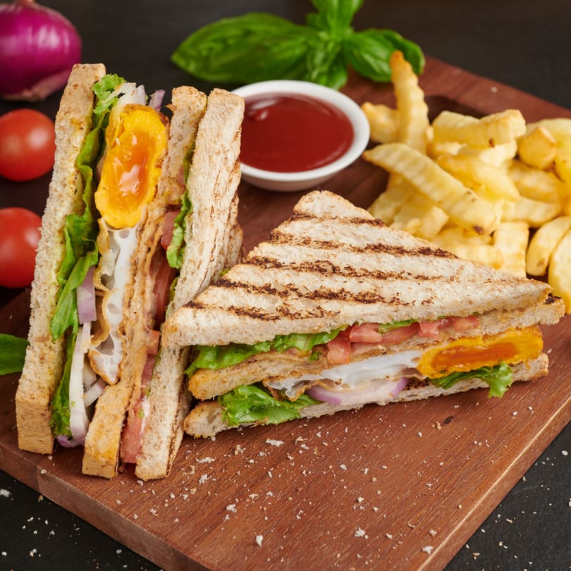 Two breakfast sandwiches with egg, lettuce, tomato, and onion, served with fries and ketchup.